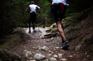 Zwei Trailrunner bewältigen einen steinigen Waldpfad mit Stöcken bergab